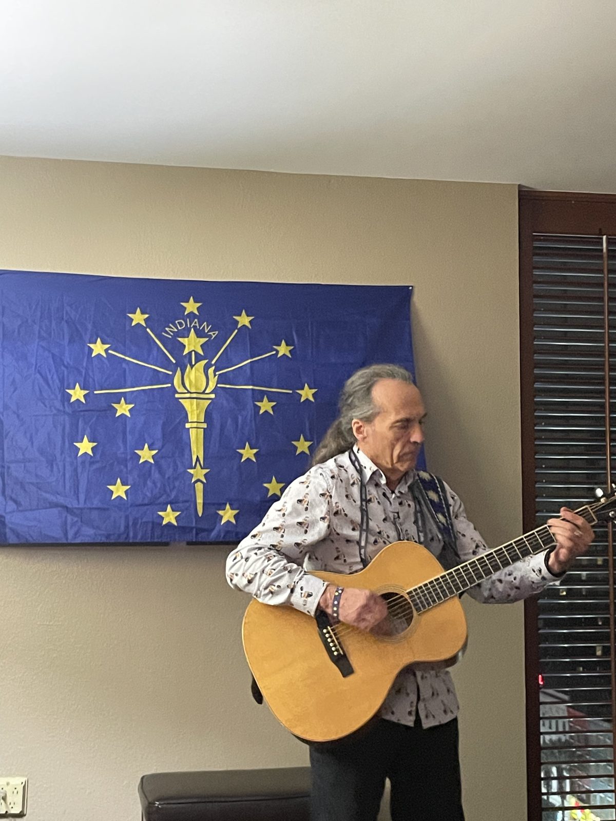 A guitarist performing beside the window under the Indiana flag