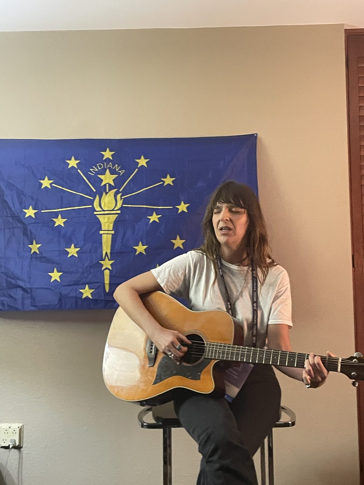 A singer with guitar performing in front of the Indiana flag