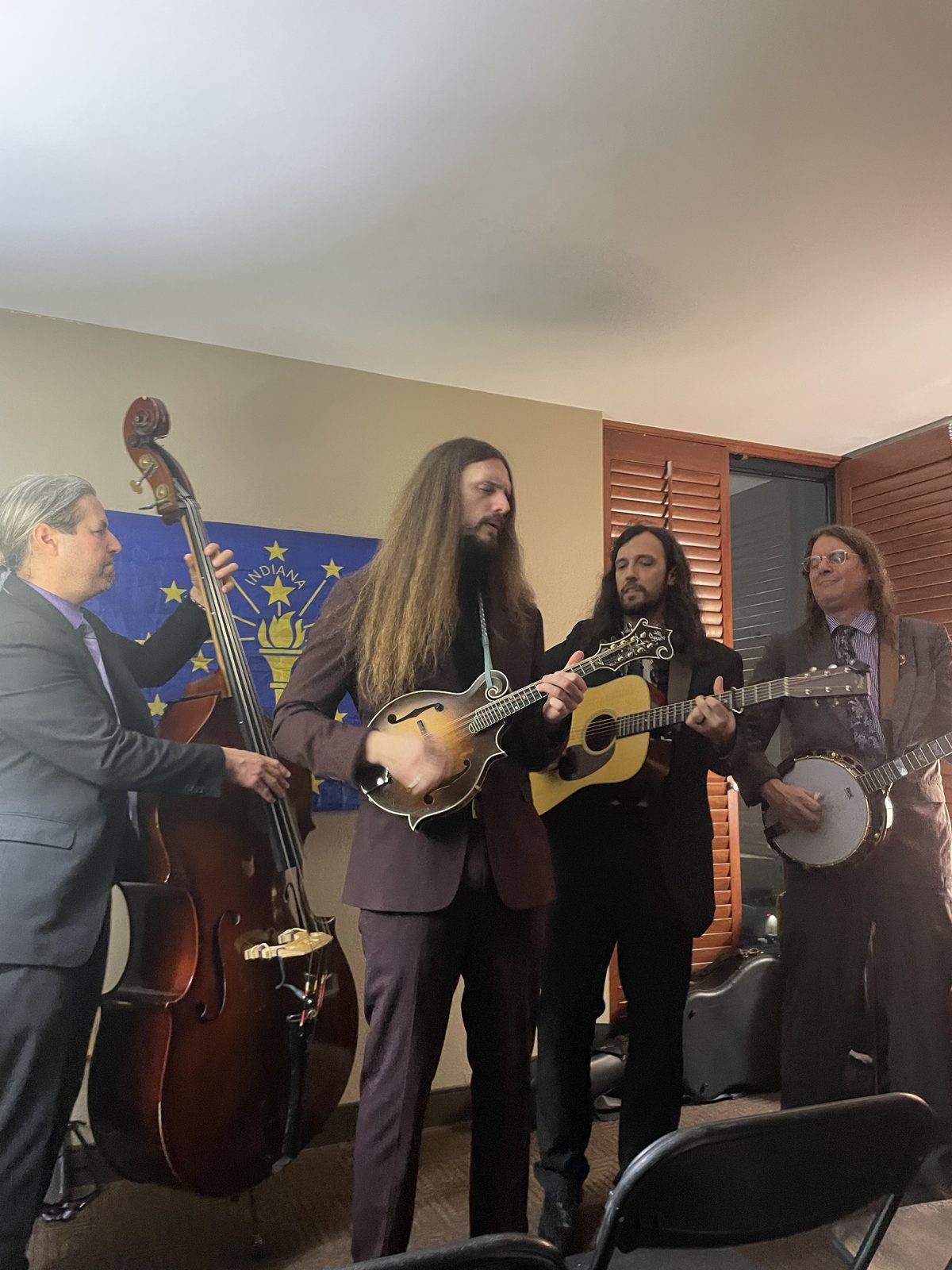 A string band with bass, mandolin, guitar, and banjo performing in front of the Indiana flag