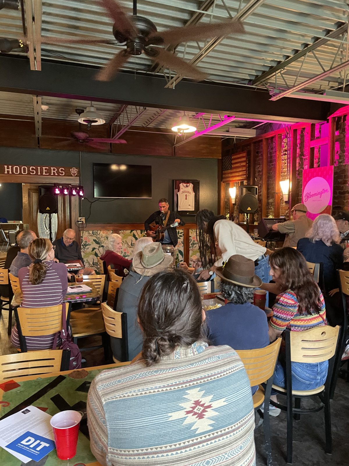 A songwriter performing to a full room at Sleeper's under pink stage lights